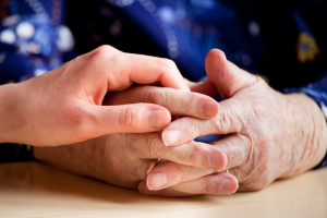 senior and caregiver holding hands